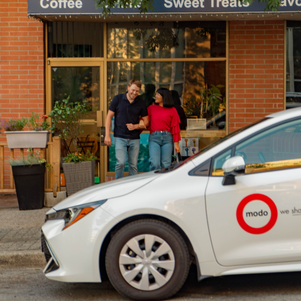 Couple leaving independent coffee shop with Modo Coop car share vehicle parked out front